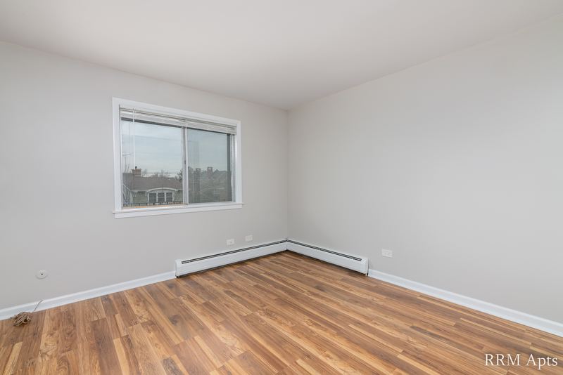 Bedroom with wood floor, one window with a brick building outside and baseboard radiator, Cook Street apartment 9
