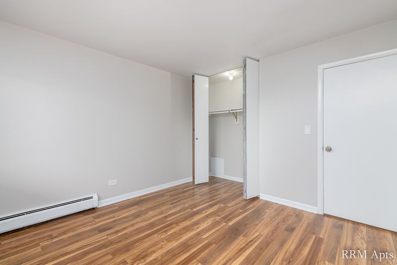 Bedroom with wood floor, an open closet with white bifold door and a white entry door, Cook Street apartment 9