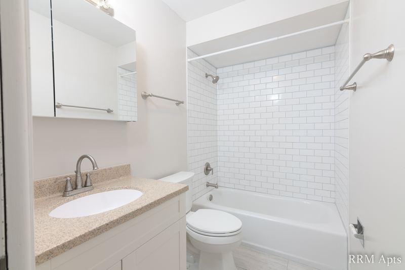 Bathroom with white subway tile tub surround, white vanity with granite-look top and toilet, Cook Street apartment 9
