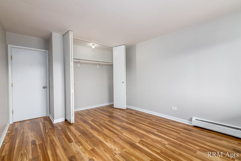 Bedroom with wood floor, two open closets with white bifold doors and baseboard radiator, Cook Street apartment 9