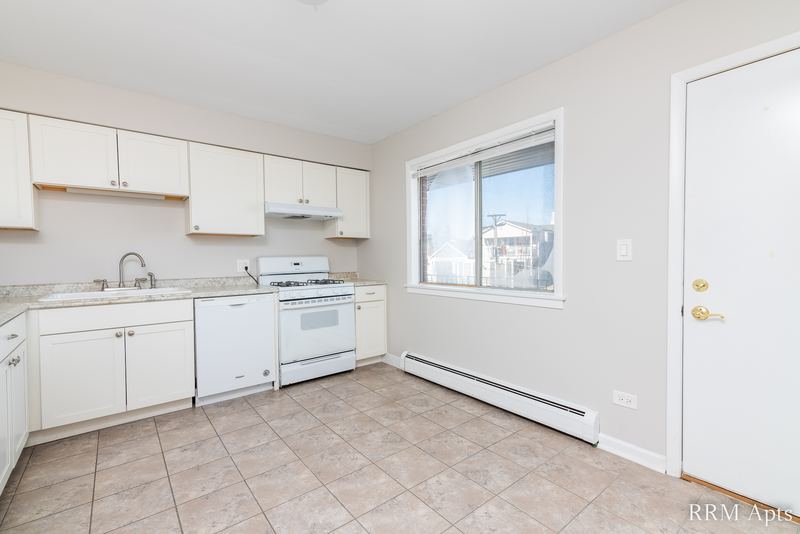 Kitchen with white cabinets, white stove and dishwasher, tile floor, window and a white entry door, Cook Street apartment 9