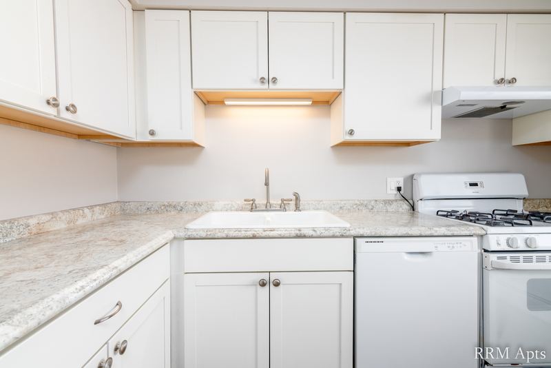 Kitchen with white cabinets, granite-look counter, sink, white dishwasher and white gas stove, Cook Street apartment 9