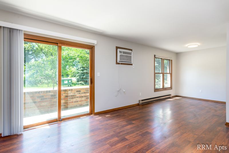 Living room with wood floor, sliding glass door, one window, wall air conditioner and radiator, Depot Road apartment 1