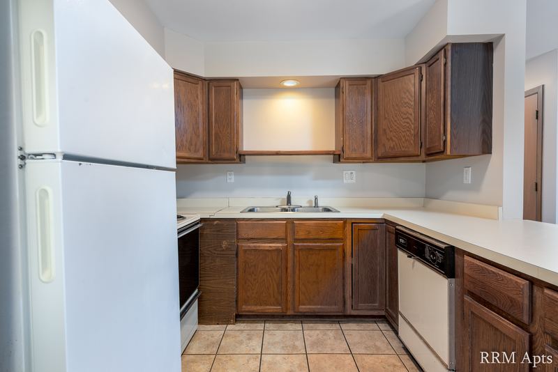 Kitchen with dark wood cabinets, white refrigerator, black stove, white dishwasher and tile floor, Depot Road apartment 1