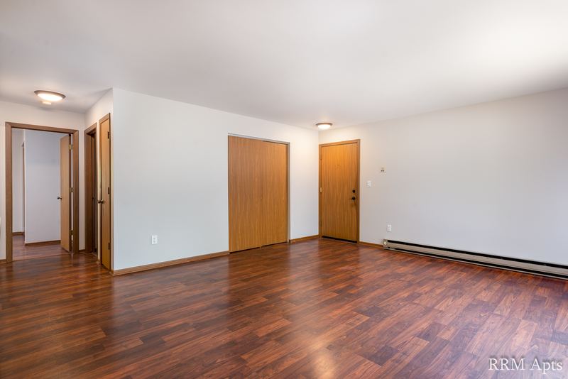 Living room with wood floor, a wood entry door and two open doorways, Depot Road apartment 1