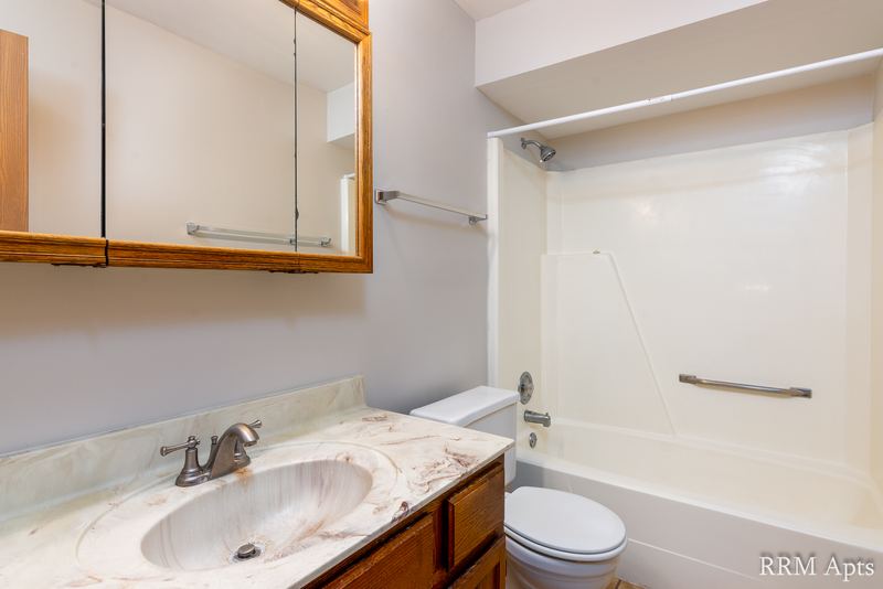 Bathroom with white tub and surround, marble-look vanity on wood cabinet, toilet and medicine cabinet, Depot Road apartment 1
