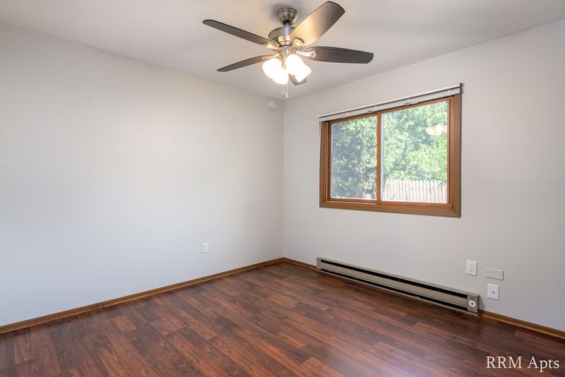 Bedroom with wood floor, ceiling fan, one wood-trimmed window and baseboard radiator, Depot Road apartment 1