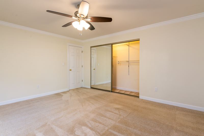 Carpeted bedroom with ceiling fan, open mirrored closet and a white door, Depot Road apartment 2
