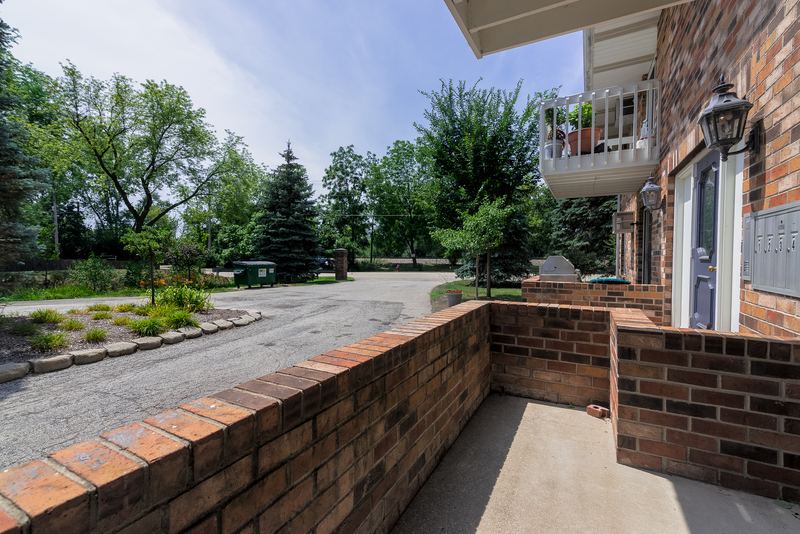 Patio with low brick wall, trees and parking area beyond, and a balcony overhead, Depot Road apartment 2