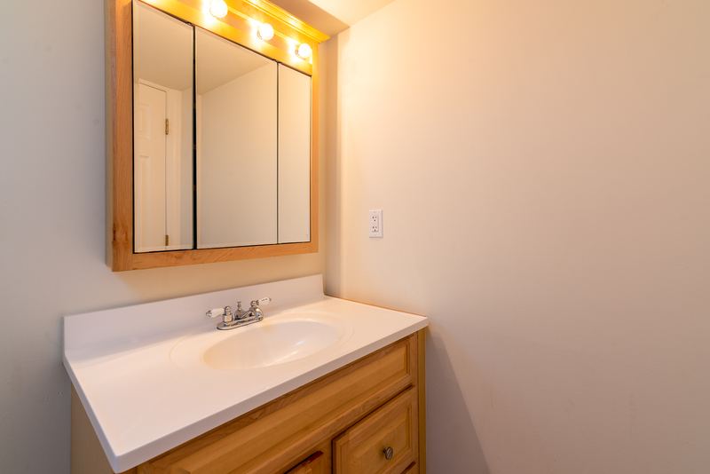Bathroom with white vanity on wood cabinet, mirrored medicine cabinet and a light bar above, Depot Road apartment 2