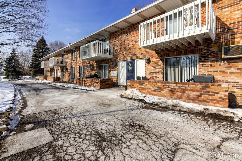 Building exterior with brick facade, white balcony railing and a snowy parking lot, Depot Road apartment 3