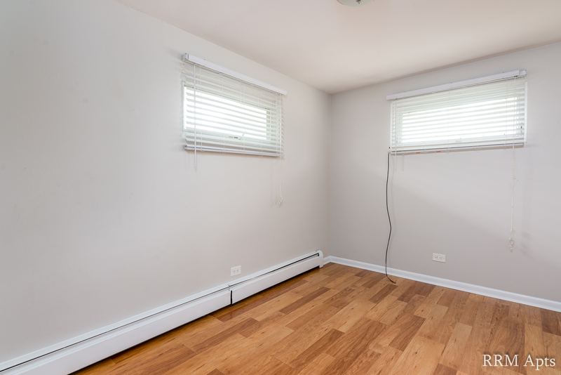 Bedroom with wood floor, two windows with blinds and baseboard radiator, East Park apartment 2