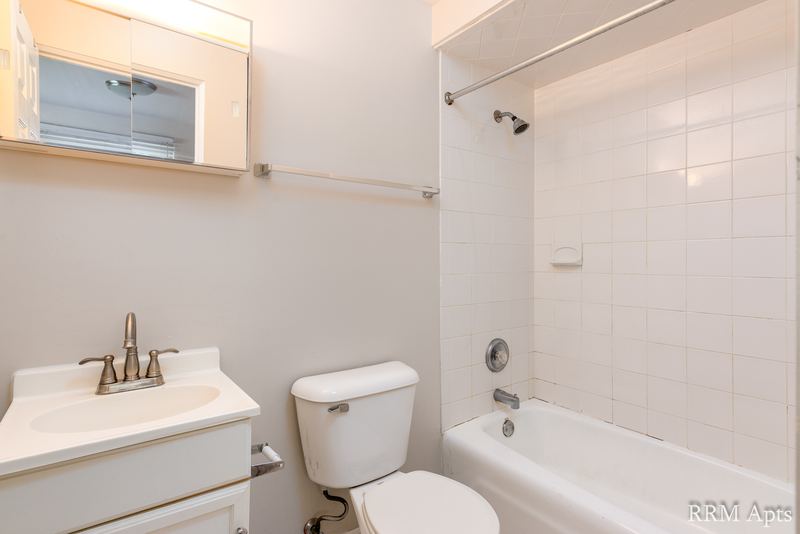 Bathroom with white tile tub surround, white vanity, toilet and a medicine cabinet, East Park apartment 2
