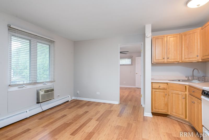 Living room with wood floor, window with wall air conditioner and an open kitchen with oak cabinets, East Park apartment 3