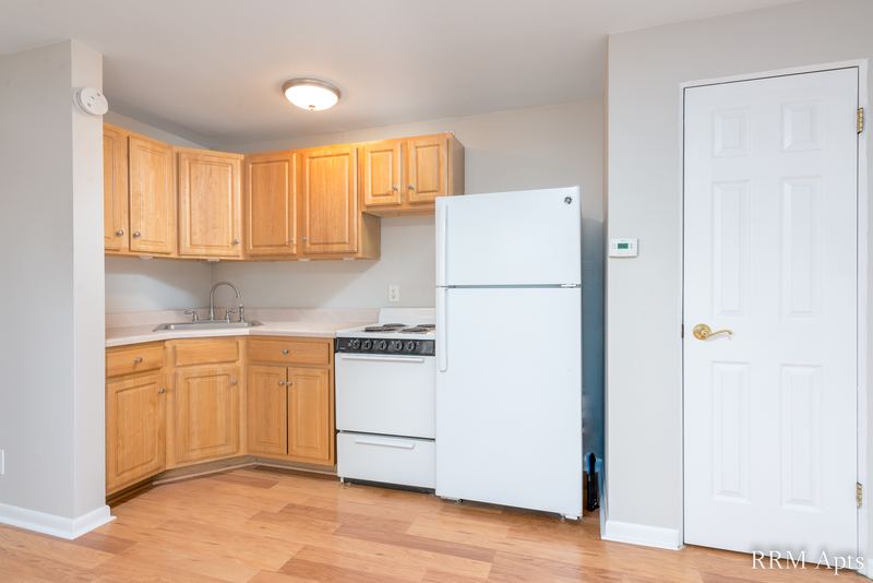 Kitchen with oak cabinets, white refrigerator, white stove and a white entry door, East Park apartment 3