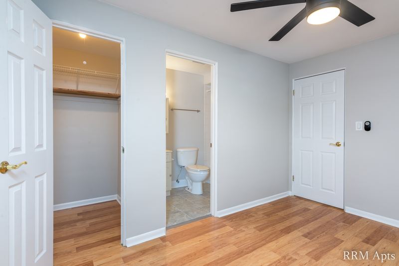 Bedroom with wood floor, ceiling fan, open closet, white doors and a doorway to the bathroom, East Park apartment 3