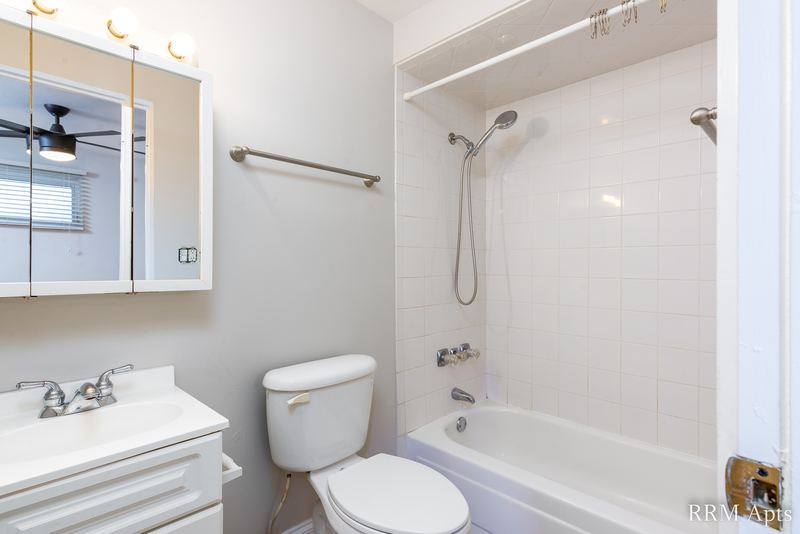Bathroom with white tile tub surround, toilet, white vanity and a mirrored medicine cabinet, East Park apartment 3