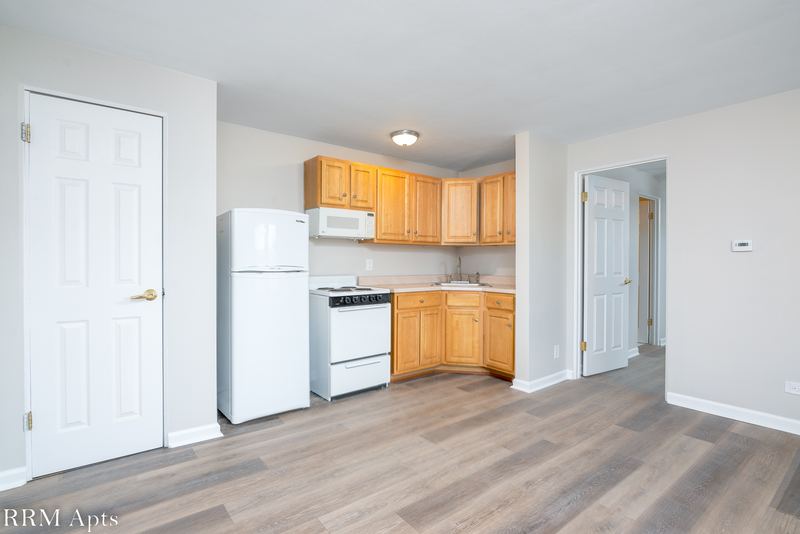 Living room with wood floor, white door and an open kitchen with oak cabinets and white appliances, East Park apartment 4
