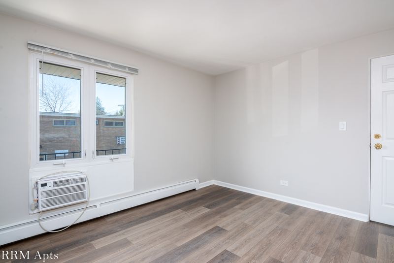 Bedroom with wood floor, one window with a wall air conditioner below it and a white door, East Park apartment 4