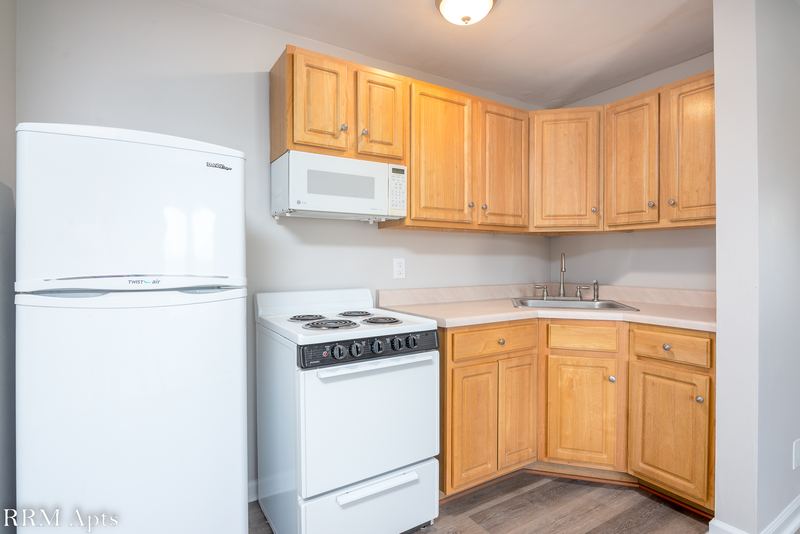Kitchen with oak cabinets, white refrigerator, white stove, over-range microwave and wood floor, East Park apartment 4