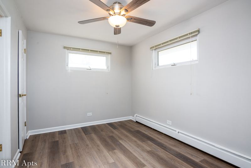 Bedroom with wood floor, ceiling fan, two small windows and baseboard radiator, East Park apartment 4