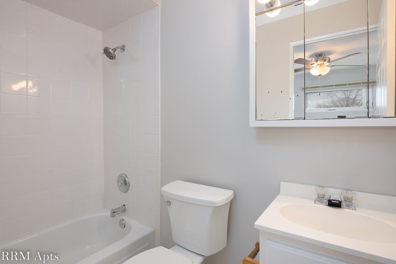 Bathroom with white tile tub surround, toilet, white vanity and a mirrored medicine cabinet, East Park apartment 4