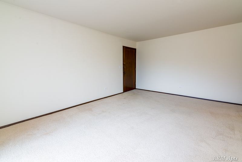Carpeted living room with cream walls and a wood door at the far end, John Mogg apartment 32927 102 S