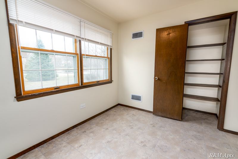 Carpeted bedroom with two wood-trimmed windows, a wood door and a closet with shelving, John Mogg apartment 32927 102 S