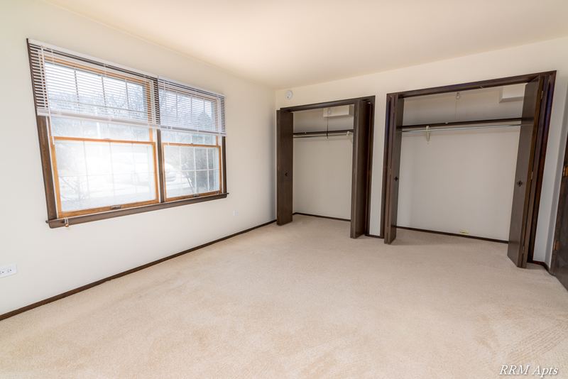 Carpeted bedroom with a wood-trimmed window and two open closets, John Mogg apartment 32927 102 S