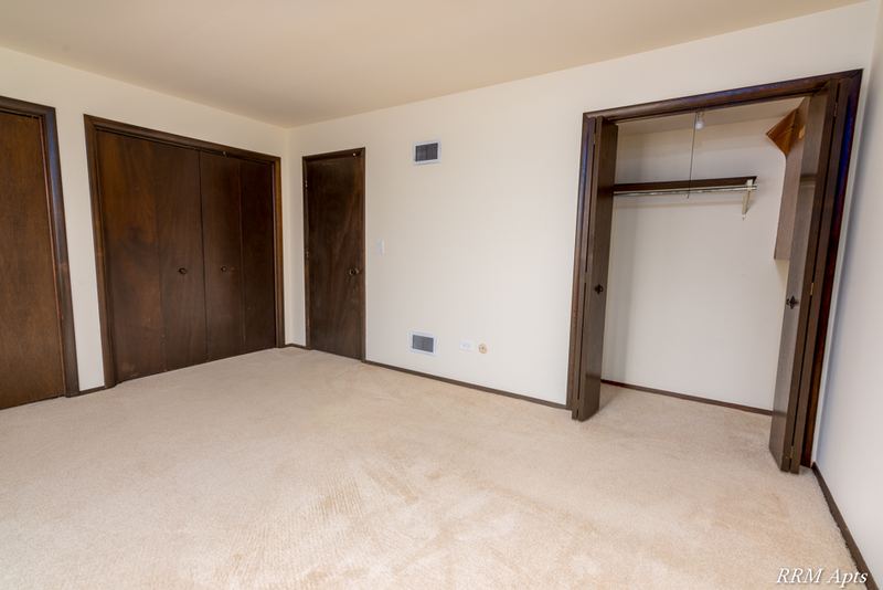 Carpeted bedroom with two wood doors and an open closet with hanging rod, John Mogg apartment 32927 102 S