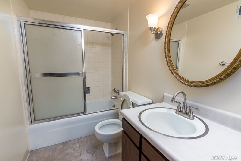 Bathroom with sliding glass tub doors, toilet, white vanity and an oval mirror, John Mogg apartment 32927 102 S
