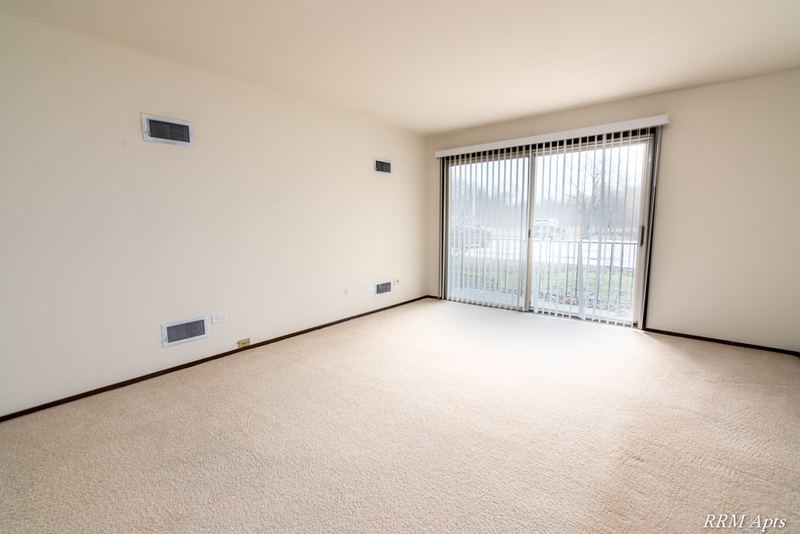 Carpeted living room with sliding glass door to a balcony and vertical blinds, John Mogg apartment 32927 102 S