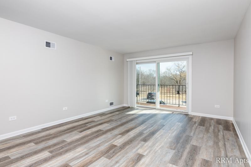 Living room with gray wood-look floor and a sliding glass door to a balcony, John Mogg apartment 32927 202