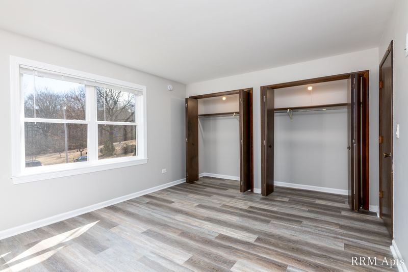 Bedroom with gray wood-look floor, a window and two open closets with wood doors, John Mogg apartment 32927 202