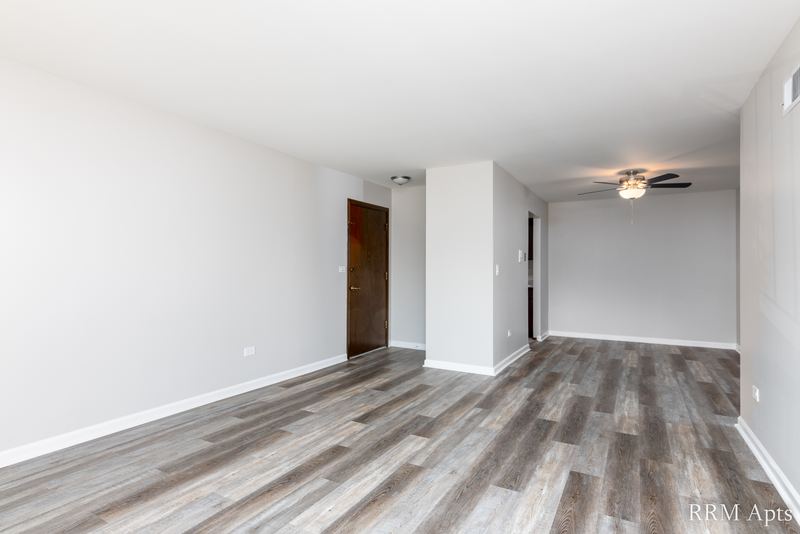 Living room with gray wood-look floor, wood entry door and a hallway beyond, John Mogg apartment 32927 202