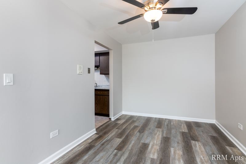 Empty room with gray wood-look floor, ceiling fan and a doorway to the kitchen, John Mogg apartment 32927 202