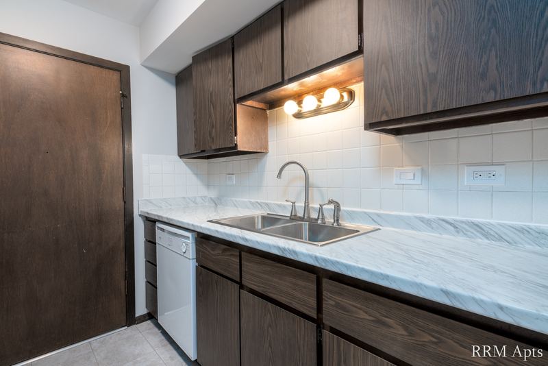Kitchen with dark wood cabinets, marble-look counter, white dishwasher and tile backsplash, John Mogg apartment 32927 202