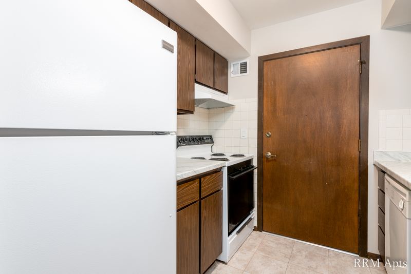 Kitchen with white refrigerator, dark wood cabinets, electric stove and a wood entry door, John Mogg apartment 32927 202
