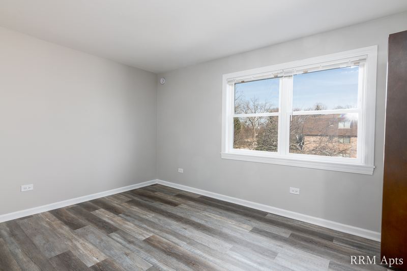 Bedroom with gray wood-look floor, one wide window and gray walls, John Mogg apartment 32927 202