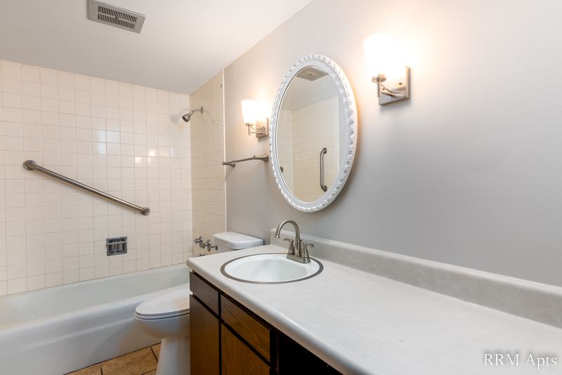 Bathroom with white tile tub surround, toilet, dark wood vanity and an oval mirror, John Mogg apartment 32927 202