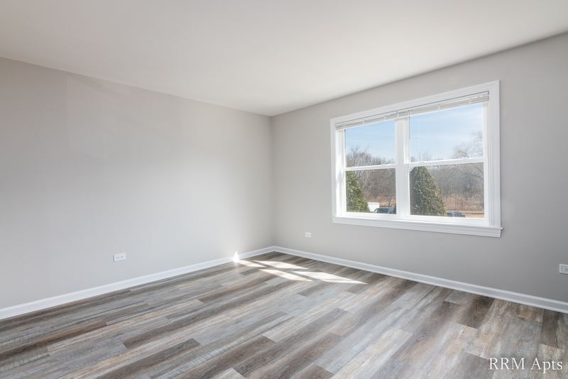 Bedroom with gray wood-look floor and a wide window looking out at trees, John Mogg apartment 32927 202