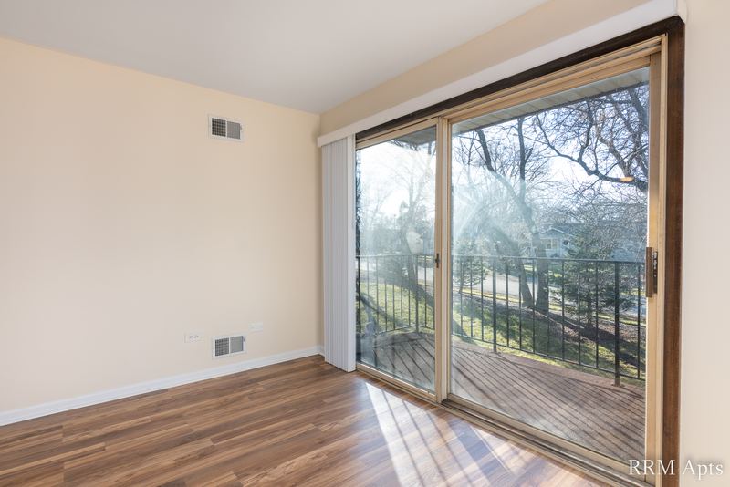 Living room with wood floor and a sliding glass door open to a balcony with iron railing, John Mogg apartment 32927 203