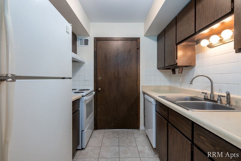 Kitchen with dark wood cabinets, white refrigerator, white stove, sink and a wood door, John Mogg apartment 32927 203