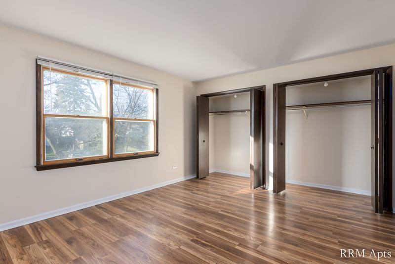 Bedroom with wood floor, a window and two open closets with dark wood doors, John Mogg apartment 32927 203