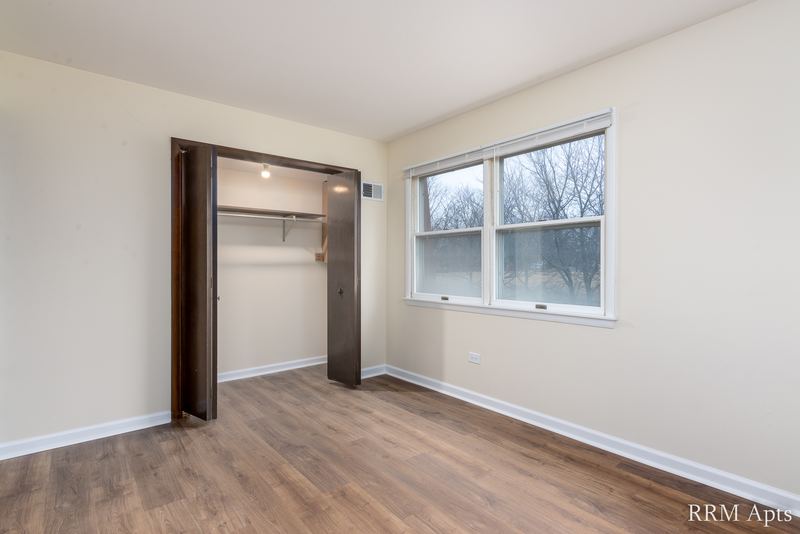Bedroom with wood floor, an open closet with dark wood door and a window, John Mogg apartment 32927 301