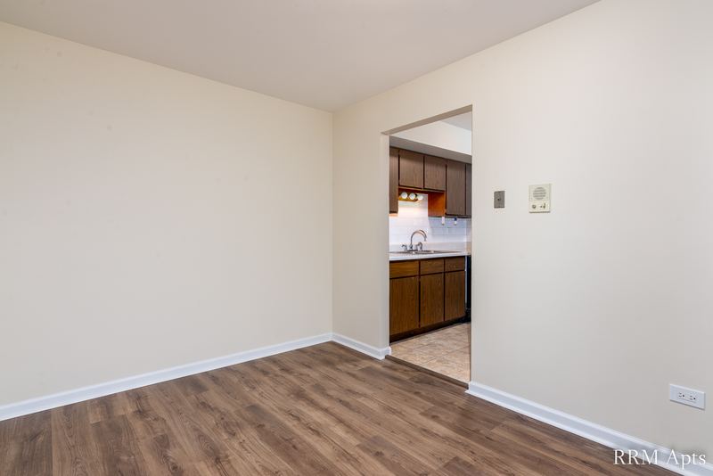 Empty room with wood floor, cream walls and a doorway to the kitchen with dark cabinets, John Mogg apartment 32927 301