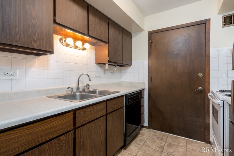 Kitchen with dark wood cabinets, double sink, black dishwasher, white stove and a wood door, John Mogg apartment 32927 301