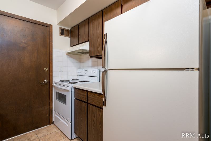 Kitchen with dark wood cabinets, white refrigerator, white electric stove and a wood door, John Mogg apartment 32927 301