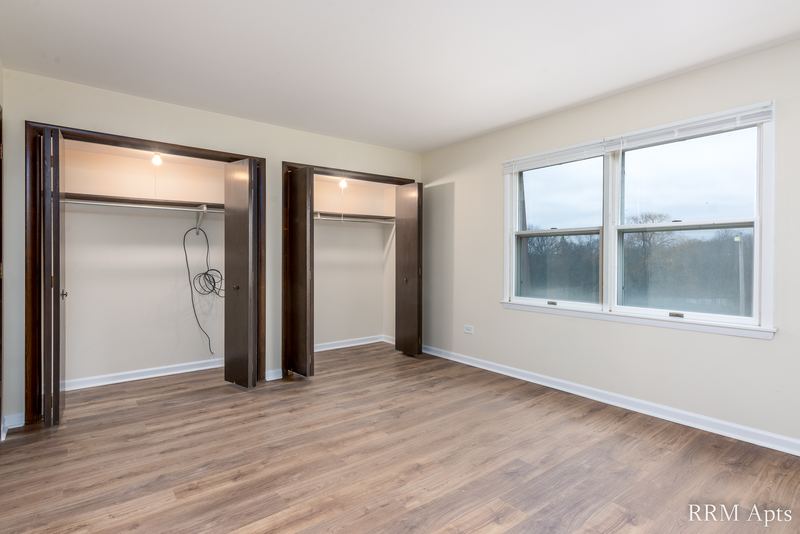 Bedroom with wood floor, two open closets with dark wood doors and a window, John Mogg apartment 32927 301