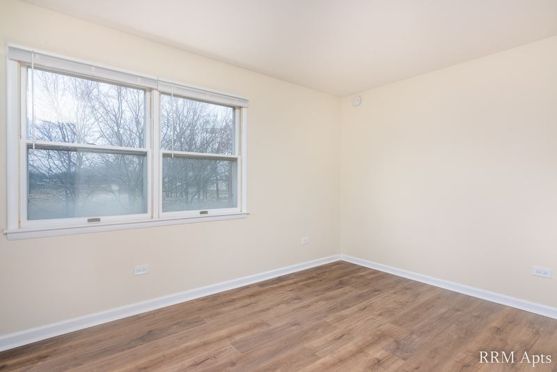 Bedroom with wood floor and a wide white-trimmed window looking out at trees, John Mogg apartment 32927 301
